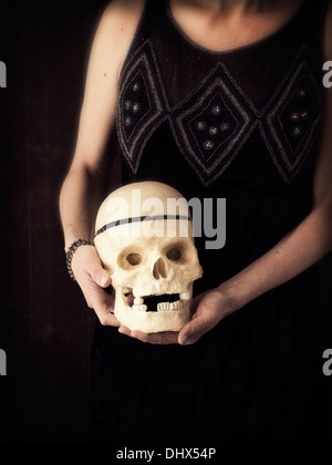 Cropped photo of a woman in vintage flapper dress holding a human skull. Stock Photo