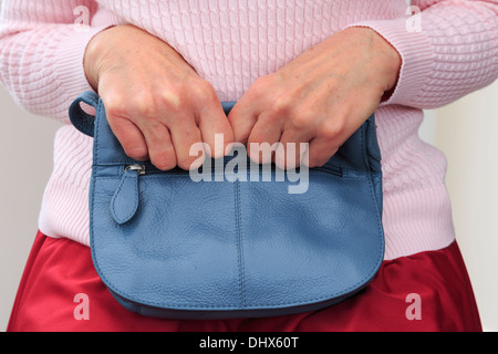 Insecure senior woman sitting and tightly clutching a handbag on her lap with two hands close to her for security. England, UK, Britain Stock Photo