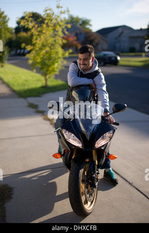 Smiling Young Man Sitting on Motorcycle in Driveway Stock Photo