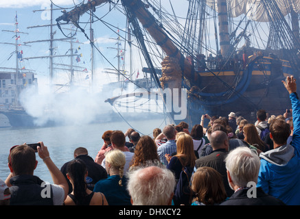 Götheborg, a sailing replica of a Swedish 18th century East Indiaman, fires her cannon with a blue plume of gunpowder smoke.
