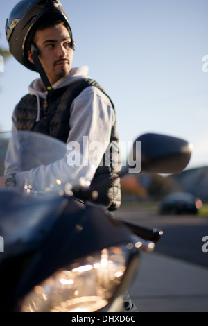 Young Man Sitting on Motorcycle with Raised Helmet on Head Stock Photo