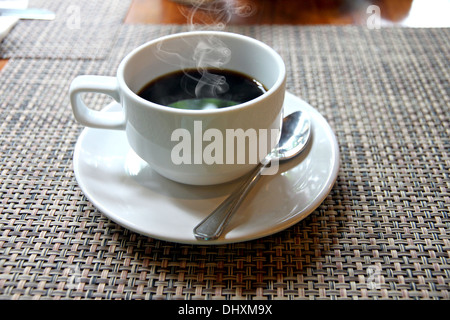 The Closeup hot Black coffee in a white cup on the table and have smoke coming out. Stock Photo