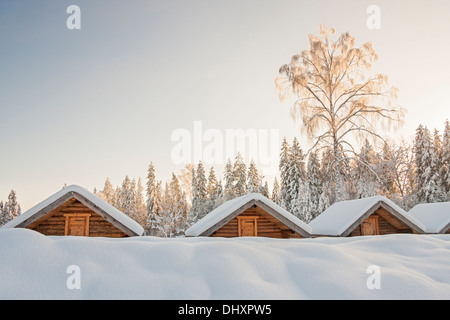 Small snowy cosy log cabins in row at very snowy winter day Stock Photo