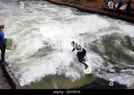 Surfers train on a man-made wave about 1 metre high in the Eisbach river in English Garden, Munich