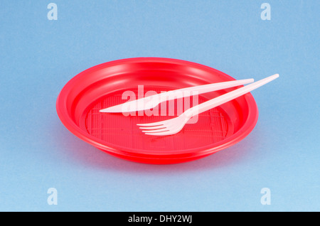 disposable plastic red plate on blue background with white fork and knife Stock Photo