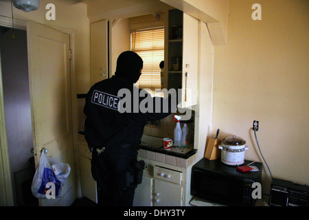 Detroit police Narcotics officer - a Narc - searches cupboards in a house during a drugs raid, Detroit, Michigan, USA Stock Photo