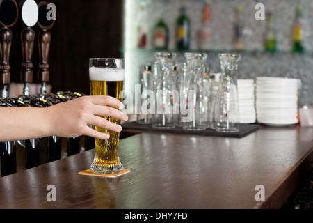 Hand of a man reaching for a pint of beer in a pub which is standing on a wooden bar counter Stock Photo