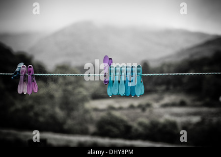Coloured clothes pegs on a washing line, dripping wet with a black & white landscape as a background. Stock Photo