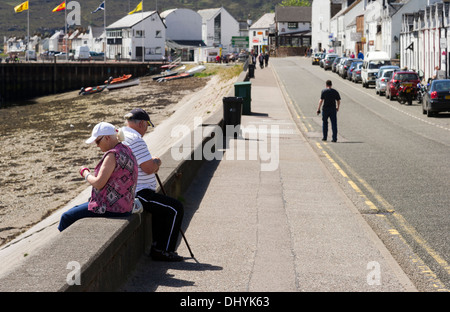 Elderly couple sitting on a concrete sea wall, Ullapool, Ross & Cromarty, West Scotland UK Stock Photo