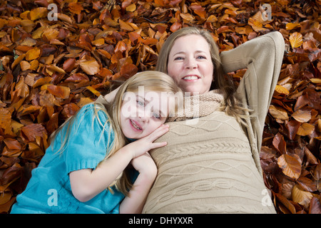Horizontal photo of a happy mother with her young daughter resting on a bed of autumn leaves Stock Photo