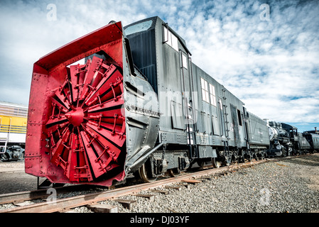 GOLDEN, Colorado - A rotary snow plow on display at the Colorado Railroad Museum in Golden, Colorado. These machines had a steam boiler and cylinders to turn the blades in front and a tender on the rear to carry the coal and water needed to fuel the boiler. The rotary plow was not self-propelled but required locomotives to push it. The big blades on the front chopped at snow and the chute directed to either side away from the tracks. Stock Photo