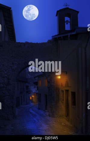 Night view of narrow street between old houses under the sky with full moon in town of Tende, France. Stock Photo