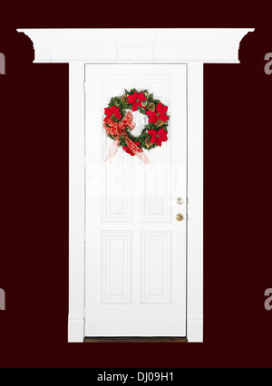 Christmas flower wreath hanging on white wood door with decorative frame, isolated over dark red Stock Photo