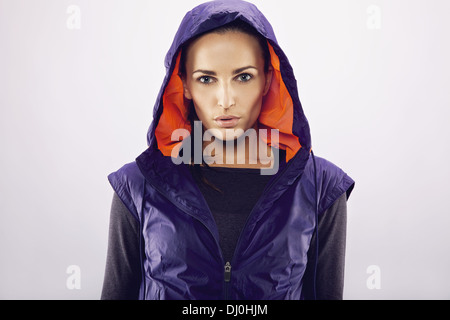 Portrait of beautiful young caucasian woman in a hooded jacket on grey background. Fitness woman in sportswear looking at camera Stock Photo