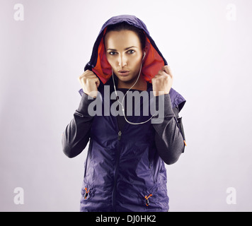Portrait of beautiful young woman in sportswear looking at camera. Confident female runner in hoodie against grey background Stock Photo