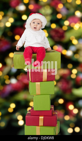 little santa baby with christmas hat seated on a big stack of gifts Stock Photo