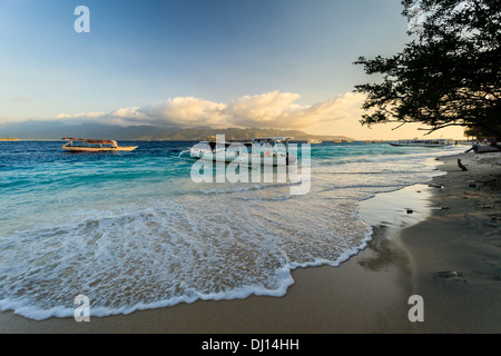 View across turquoise water to Lombok Island from Gili Trawangan beach at sunset with boats moored on the coast Stock Photo
