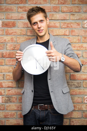 Young businessman holding a clock on brick wall background. Time in business concept Stock Photo