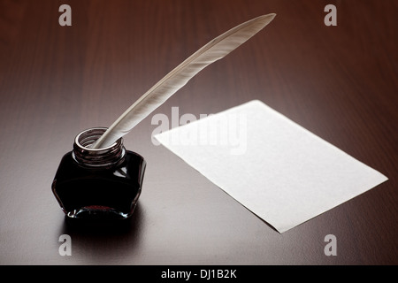 Ink, quill and an empty page on brown desk Stock Photo