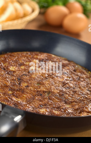 Preparing Spanish tortilla (omelette with potatoes) in frying pan with eggs and bread slices in the back Stock Photo