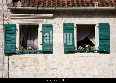 Green shuttered windows on old stone house with flowers in window Stock Photo