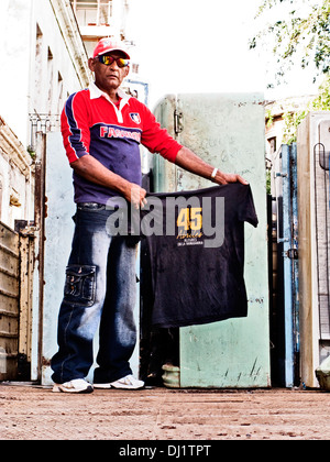 Cuban man wearing sunglasses and a cap, standing up holding a t-shirt Stock Photo