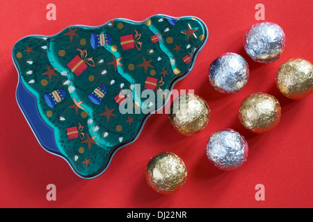 Christmas tree tin with foil covered chocolate balls - chocolates ready for Christmas isolated on red background Stock Photo