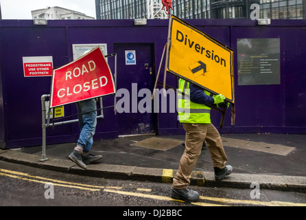 Two workmen move Road Closed and Diversion signs near a construction site in central London, UK. Stock Photo