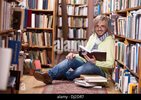 Handsome man reading book while sitting on floor in library Stock Photo