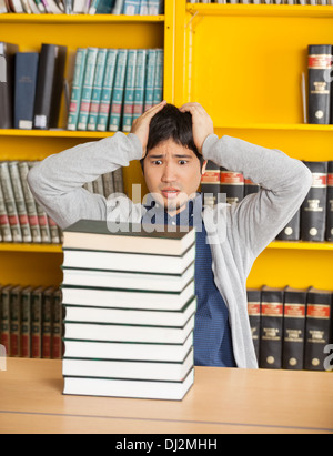 Confused Man Looking At Stacked Books In Library Stock Photo