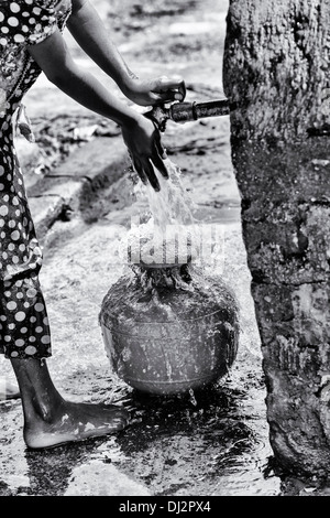 Indian girl filling a plastic pot with water from a standpipe in a rural Indian village. Andhra Pradesh, India. Black and White. Stock Photo