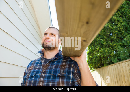 Carpenter Carrying Plank On Shoulder At Construction Site Stock Photo