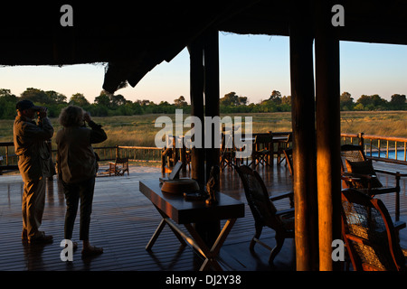 A couple of tourists on the porch outside the camp Khwai River Lodge by Orient Express in Botswana, within the Moremi Game Reser Stock Photo