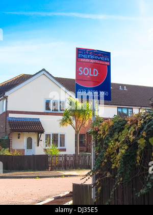 A house and typical street in England with an estate agents sold sign visible Stock Photo