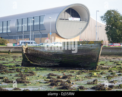 An rotting wooden boat at low tide with the Mountbatten leisure centre in the background. Portsmouth, England Stock Photo