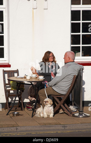 senior couple sitting at table outside for drinks with dog at Weymouth in November Stock Photo