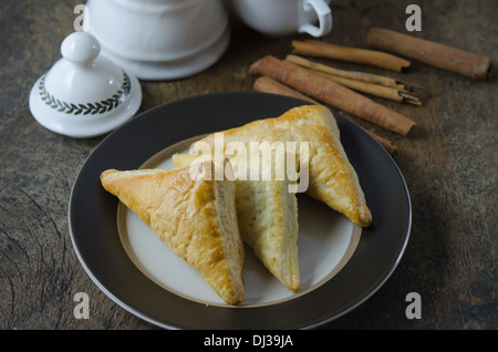 Puff pastry on the plate with cinnamon sticks over wooden background Stock Photo