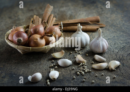 onion and cinnamon stick in basket , garlic and peppercorns on wooden board ( food ingredients ) Stock Photo