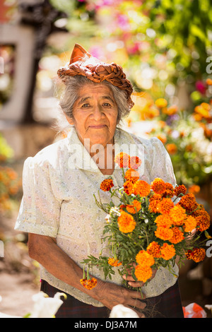 An elderly Zapotec woman smiles as she places fresh flowers on the grave of a family member for the Day of the Dead festival. Stock Photo