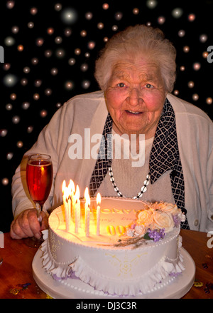 100 years old celebrations Happy alert elderly lady at 100 years of age with her birthday cake and a glass of pink champagne. 100 lights in background Stock Photo