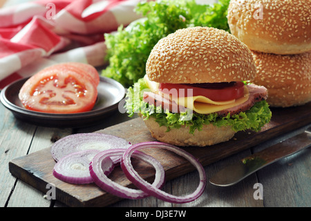 Sandwich with ham, cheese, tomato and lettuce on wooden cutting board closeup Stock Photo