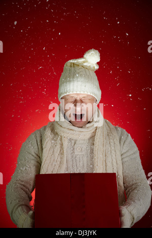 Portrait of surprised man in winterwear holding open giftbox with snowflakes flying out of it Stock Photo