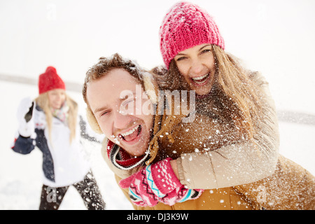 Portrait of happy young couple looking at camera in winter park with their friend behind Stock Photo