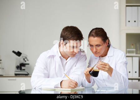 Two scientists looking at glass flask with liquid oil in laboratory while analyzing its characteristics Stock Photo
