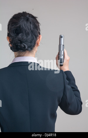 Back of woman in business suit holding a hand gun pointing up Stock Photo