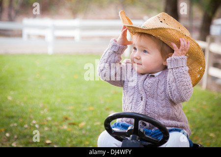 Happy Young Toddler Wearing Cowboy Hat and Playing on Toy Tractor Outside. Stock Photo