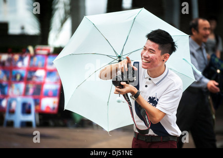 Young guy holding an umbrella takes photos during a storm in Hong Kong Stock Photo
