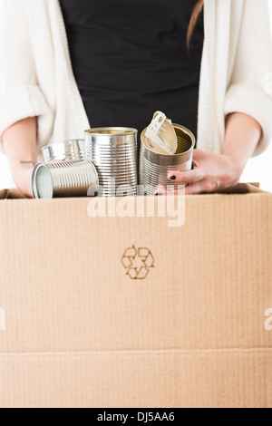 Hands of woman placing metal cans in cardboard box for recycling Stock Photo