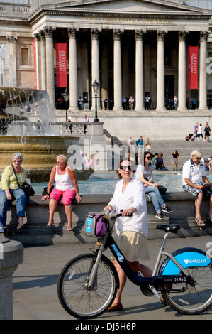 London, England, UK. Trafalgar Square - woman pushing a 'Boris Bike' - cycle for hire Stock Photo