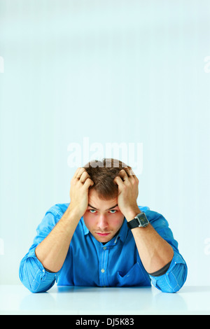 Young depressed businessman sitting at the table and looking at camera in office Stock Photo